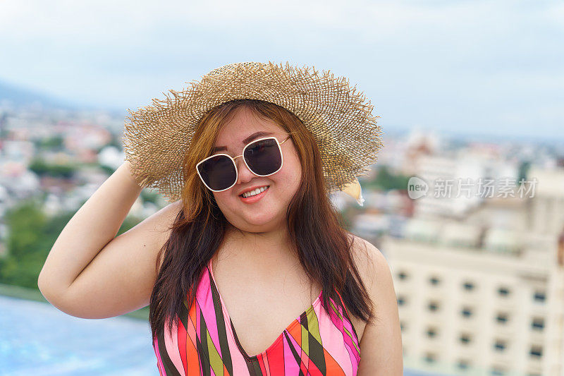 超重的年轻亚洲妇女穿着橙色swimsuitÂ和稻草沙滩太阳帽在游泳池放松快乐加码妇女愉快有趣的假期旅行在夏天。