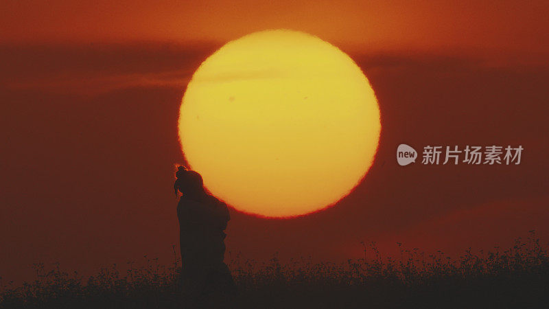 夕阳下，母亲抱着婴儿，背景是橙色的天空