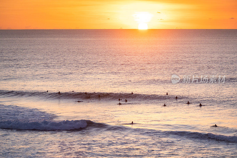日落冲浪:黄金时间海景与剪影冲浪者骑浪，平静的大海和温暖的天空。