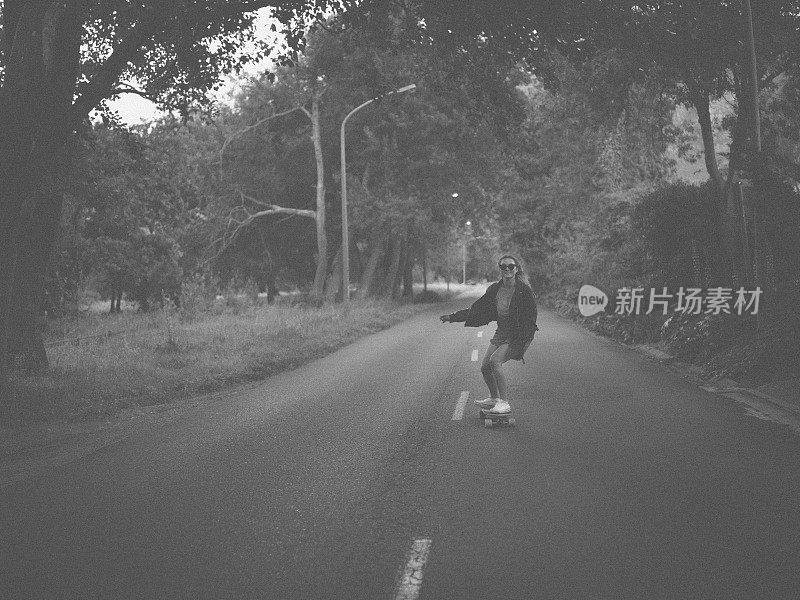 十几岁的女孩骑着滑板沿着绿树成荫的道路