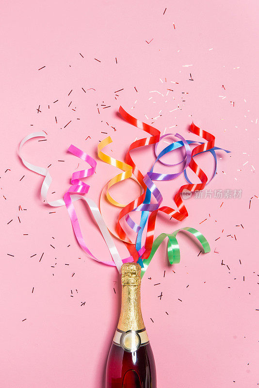 粉红色背景上有彩色派对彩带的香槟酒瓶。