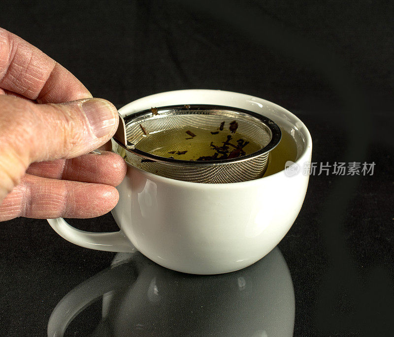 泡茶器和茶杯，手放在黑色背景上