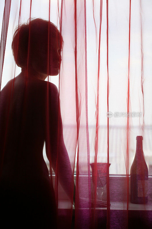 红色窗帘后的窗户上，漂亮女人的剪影。玻璃。瓶子。