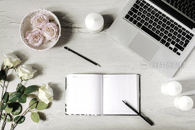 现代风格的工作场所，笔记本电脑，日记本，白色蜡烛，玫瑰和木制办公桌。平躺
