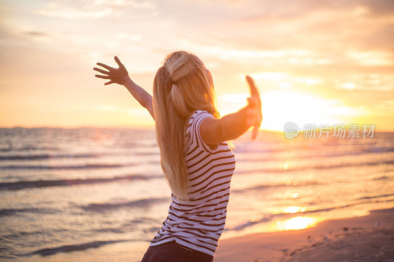 欢呼的女人在海边向夕阳张开双臂