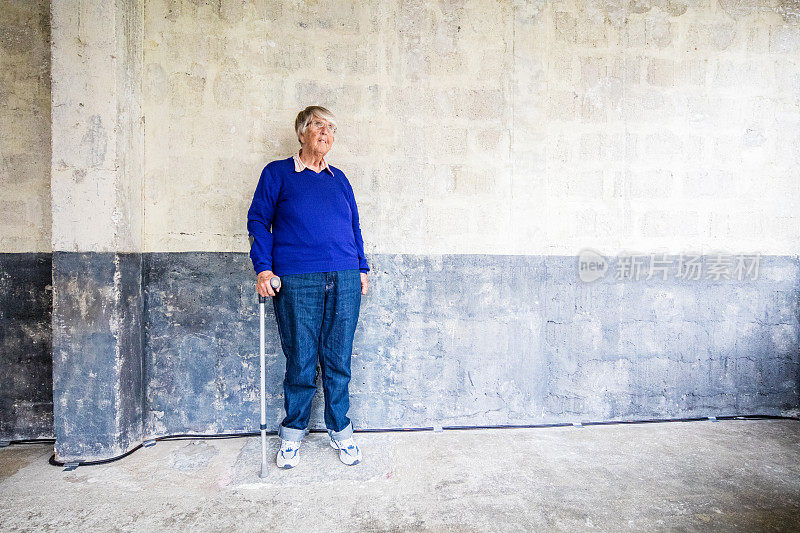 老妇人拄着拐杖站在墙上