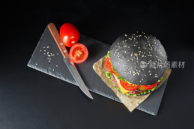 黑色汉堡与番茄和刀孤立在黑色背景。