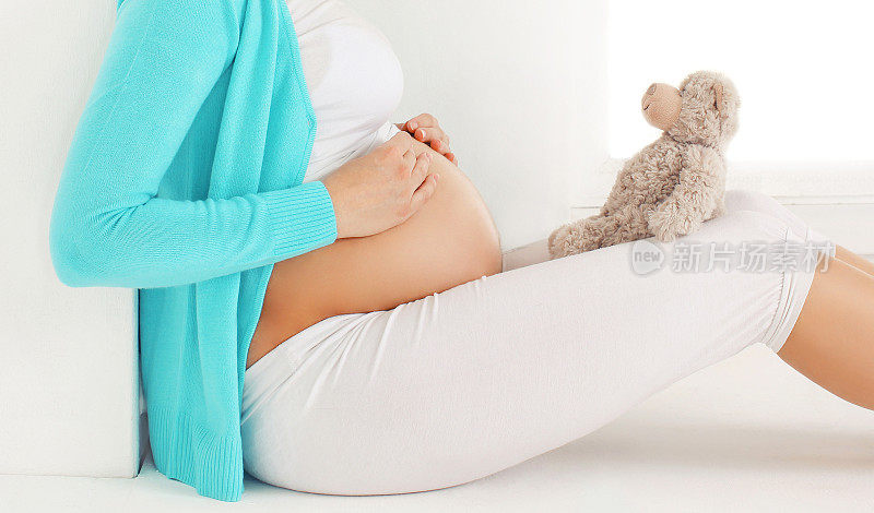 孕妇坐在泰迪熊旁边梦想着未来的孩子