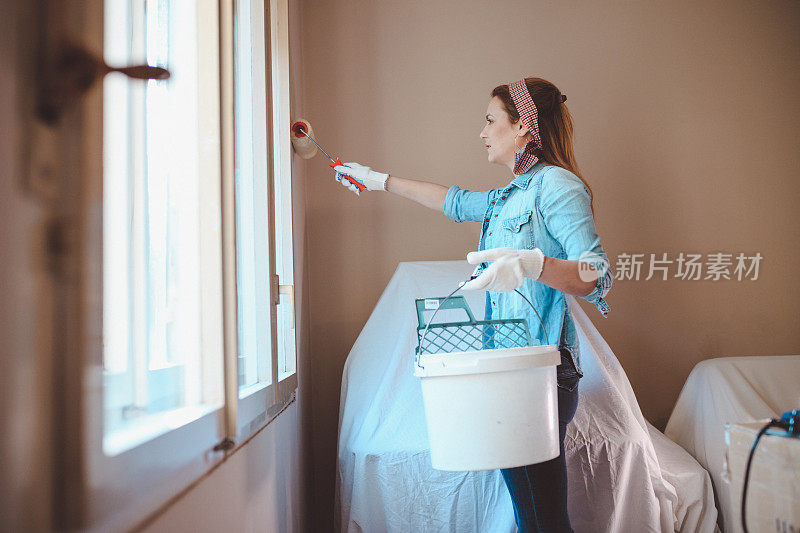 在公寓里用油漆滚筒刷墙的女人