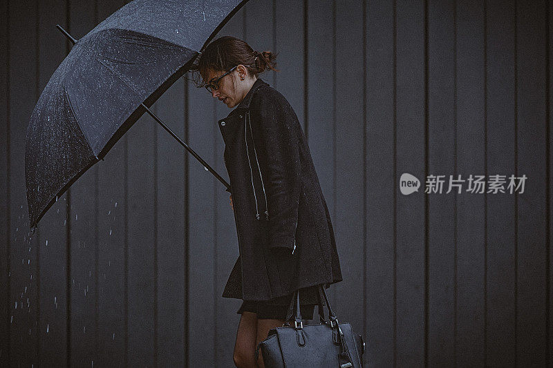 一名年轻女子撑着伞，在寒冷的秋日里在风雨中行走。