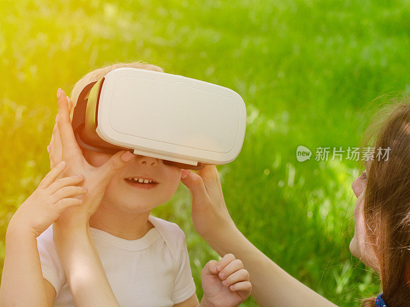 妈妈在绿草的背景下纠正儿子的虚拟现实眼镜