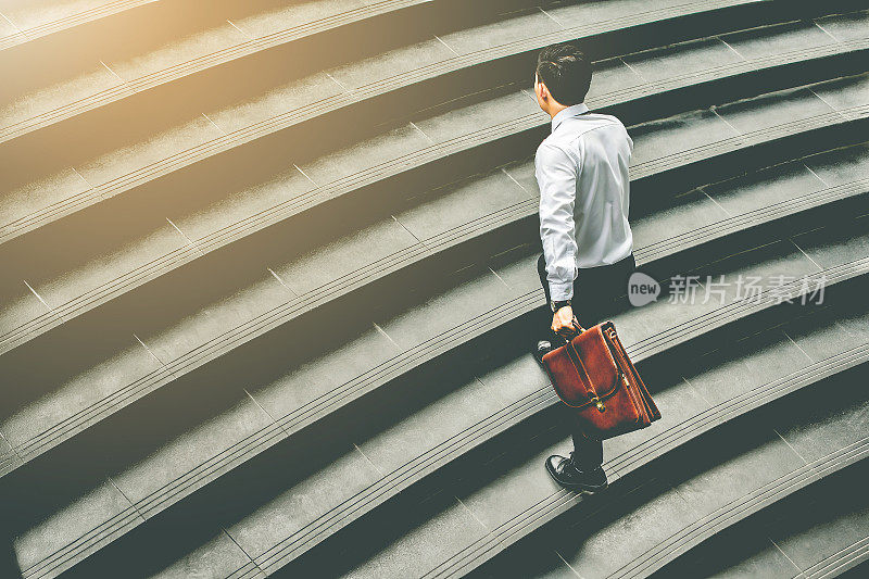 年轻的亚洲商人拿着棕色皮包在楼梯上工作去办公室匆忙的工作时间与日落顶视图和复古色调