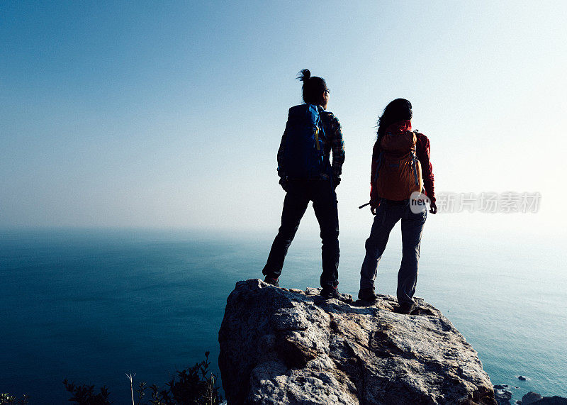 两个女徒步旅行者在海边看风景，山顶岩石边缘