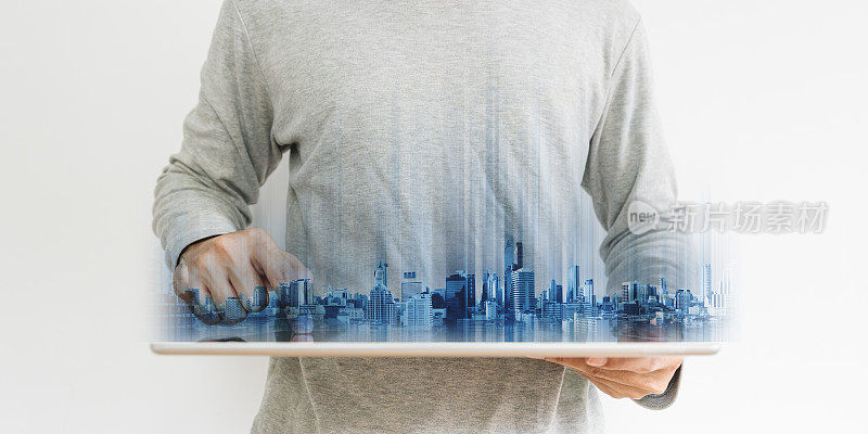 商人穿着休闲服装使用数字平板电脑，与未来主义的现代建筑全息图，在白色背景上。房地产和技术概念