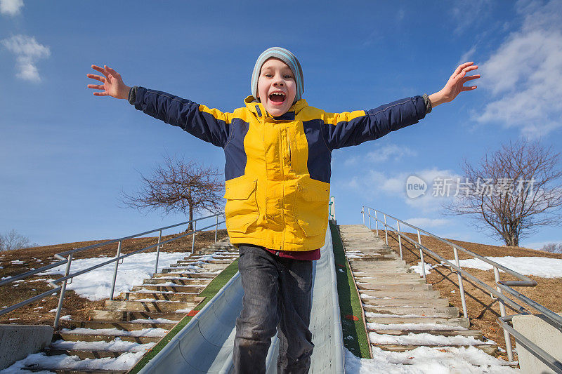 快乐的男孩从操场上的滑梯上跳下来