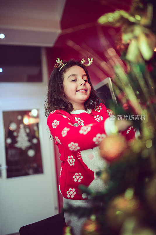 可爱的小女孩用圣诞装饰品装饰她的冷杉树