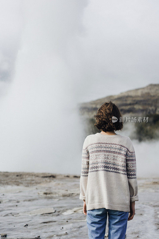 一个女人站在冰岛的间歇泉旁