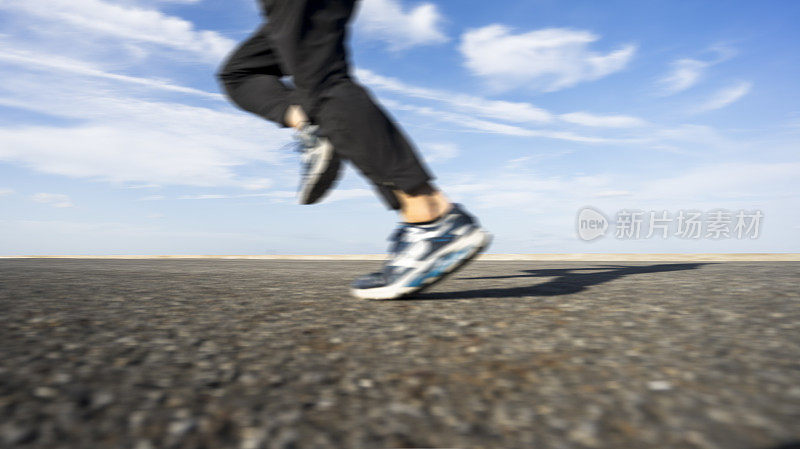 年轻的男运动员在柏油路上迎着天空奔跑