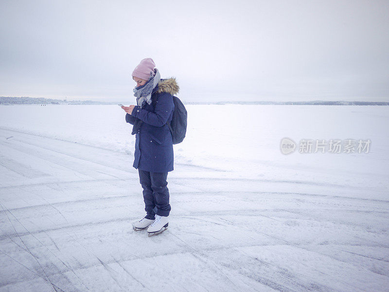 芬兰的生活方式，年轻女子在冰湖上滑冰时查看手机