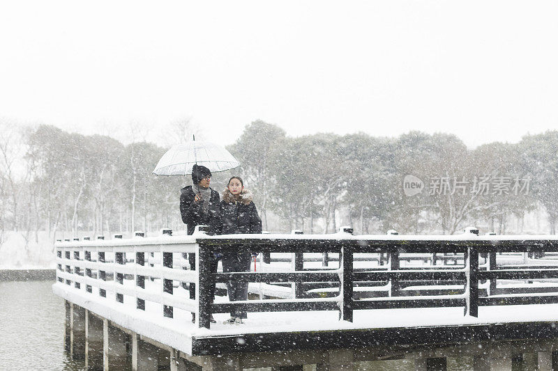 一对情侣撑着伞站在白雪覆盖的木桥上