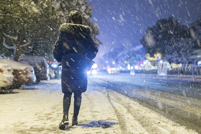 后视图的女人走在街上的晚上在雪