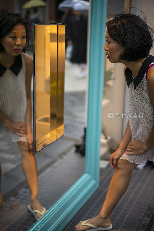 日本京都大街上，一名女子站在带有镜子的窗户前。
