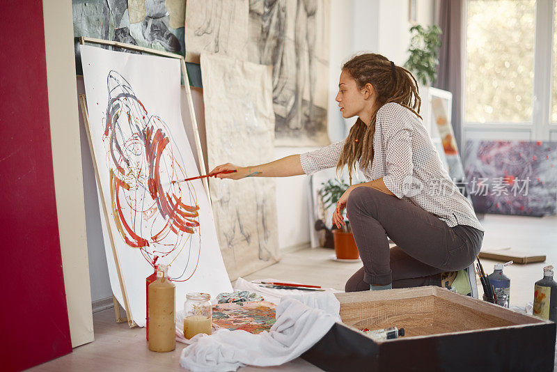 艺术女孩坐在画室里，在画架上画画。