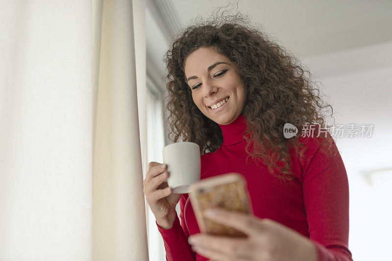 漂亮的年轻女子一边喝咖啡一边玩智能手机