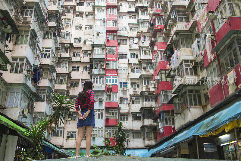 亚洲女性在城市环境中，周围是香港的旧住宅公寓，看着别处思考