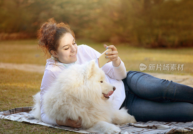 女人和萨摩耶狗(秋天，智能手机)