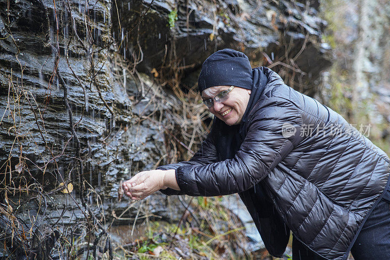 这位成熟的女性，游客，用山上小瀑布的天然水洗脸洗手。