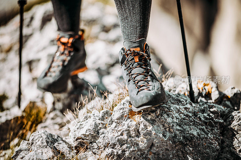 穿着登山靴和手杖的登山者的腿，站在岩石上