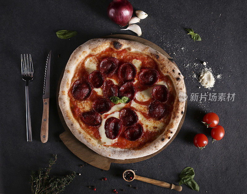 美味的意大利辣香肠披萨和烹饪原料西红柿罗勒在黑色混凝土背景。俯视图热香肠披萨。与复制空间的文本。平躺