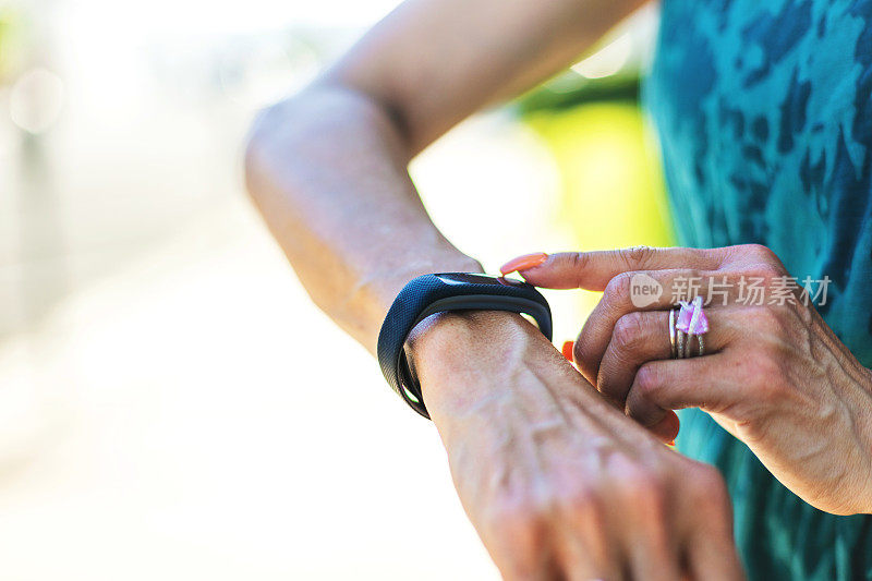 成熟的成年女性在户外运动时用智能健身追踪器检查心率