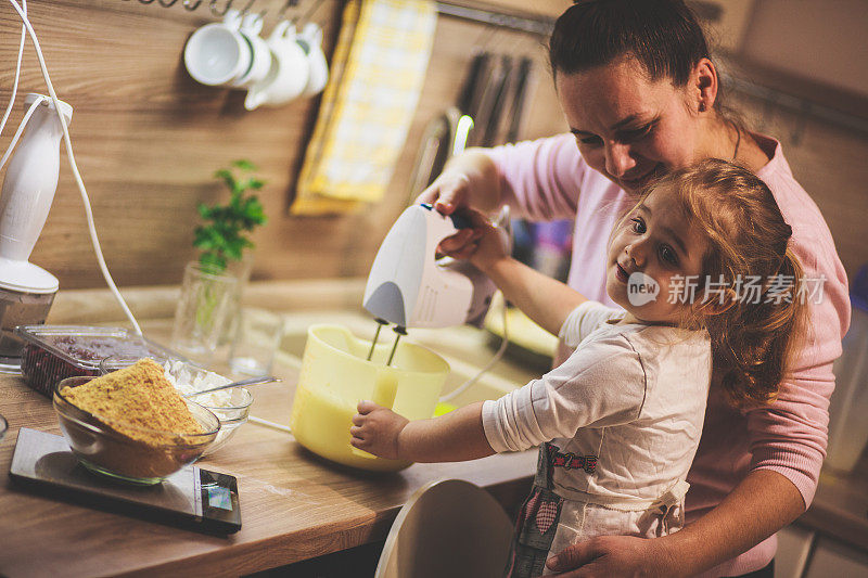 快乐的小女孩正在和妈妈一起搅拌蛋糕面糊