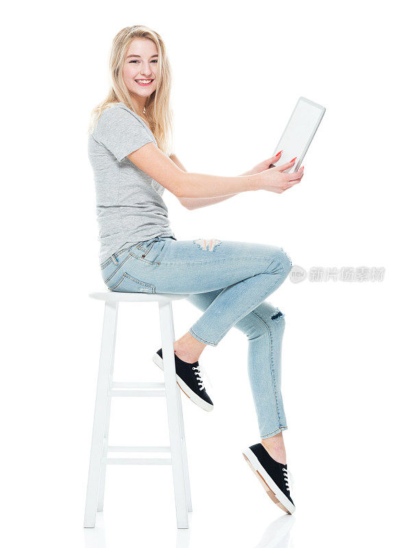 z一代女性穿着牛仔裤坐在白色背景前，使用着平板电脑