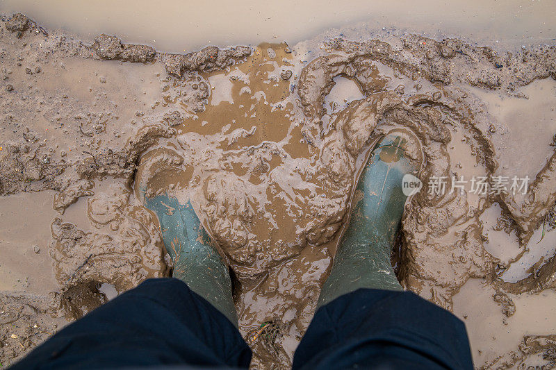 脚在绿色橡胶靴子站在潮湿的棕色泥直接俯瞰