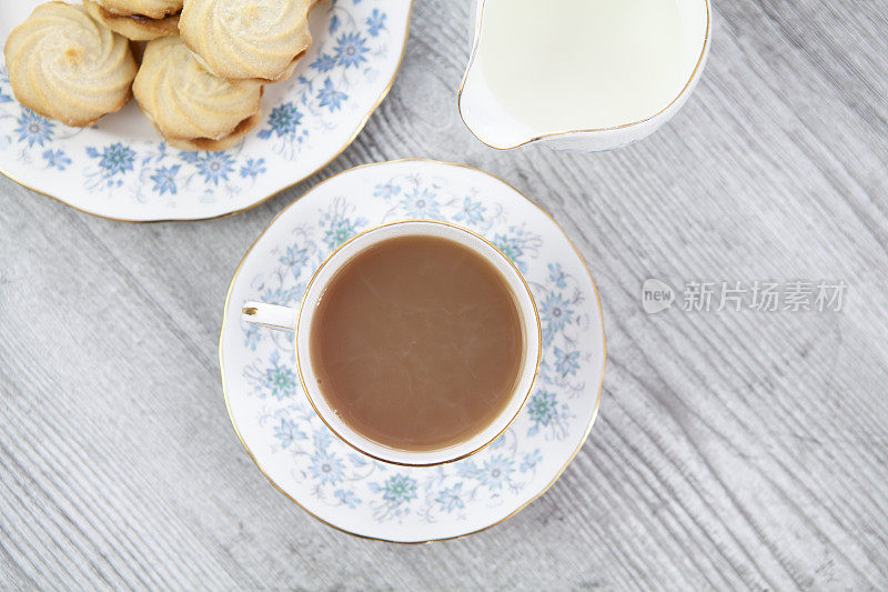 一杯茶，一个牛奶壶和一盘维也纳菜在一个轻木制的表面上旋转