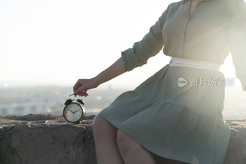 一个女人手里的黑色闹钟以自然为背景。永恒和时间的概念