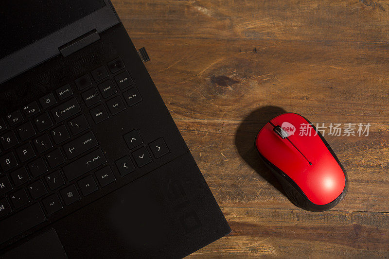 木制书桌上放着笔记本电脑和红色鼠标。