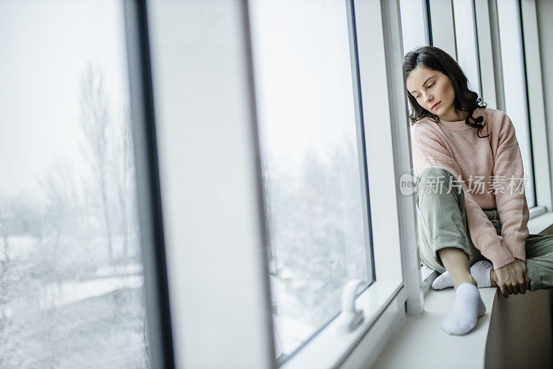 抑郁的女人在家里感到难过。女人悲伤地看着窗外。沮丧孤独的女人独自站在窗前看着窗外。