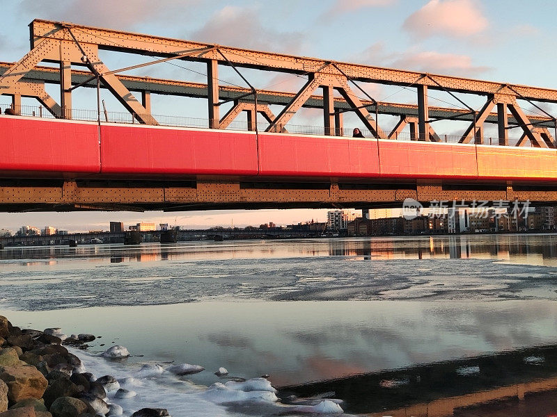 丹麦日落时冰冻的水面上的红色人行天桥