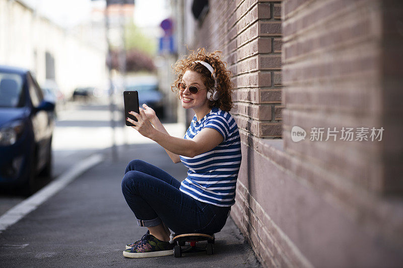 玩滑板的女孩用耳机打电话。库存图片