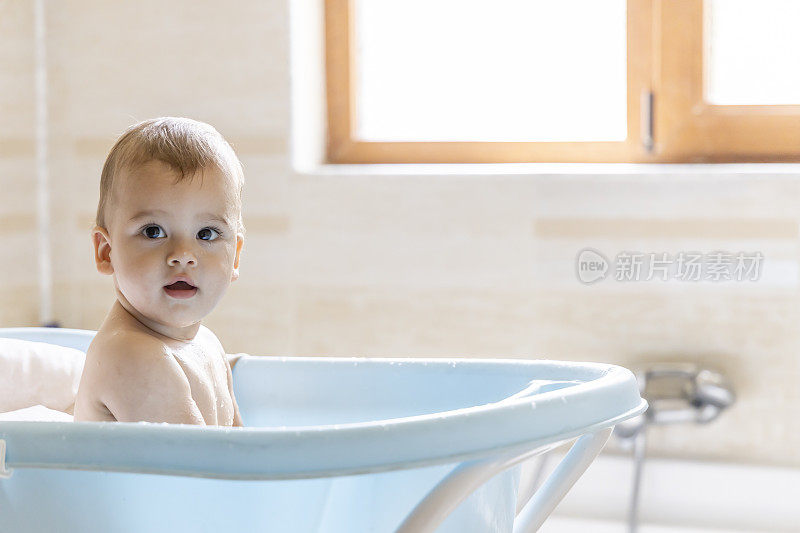 一个可爱的婴儿正在浴盆里洗澡。洗澡时泼水的婴儿