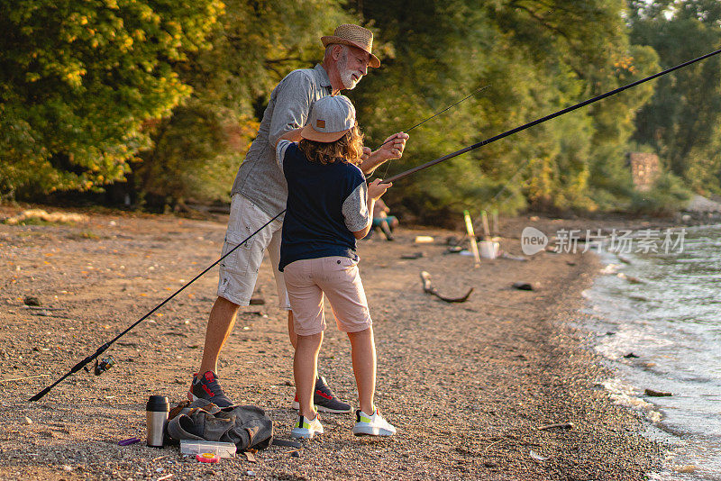 可爱的小男孩，帮他的爷爷把鱼饵绑在鱼竿上，两人都在河边享受周末的冒险
