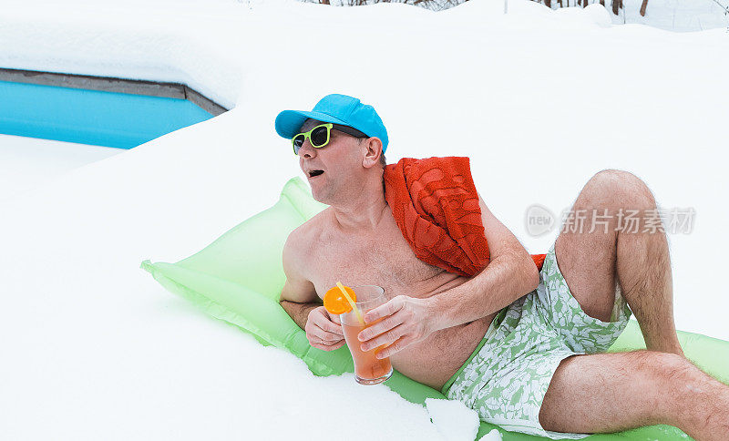 一个穿着泳裤的年轻人躺在厚厚的雪地里的充气床垫上。一个男人正在一个覆盖着雪的室外游泳池旁休息。