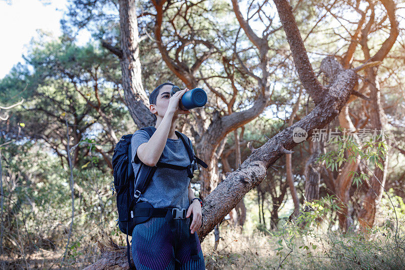 年轻的秃顶女子在森林里徒步旅行时喝水