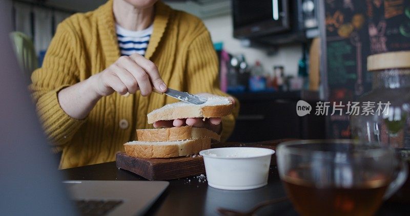 一个成熟的女人坐在厨房的桌子旁，边喝茶边用笔记本电脑做早餐