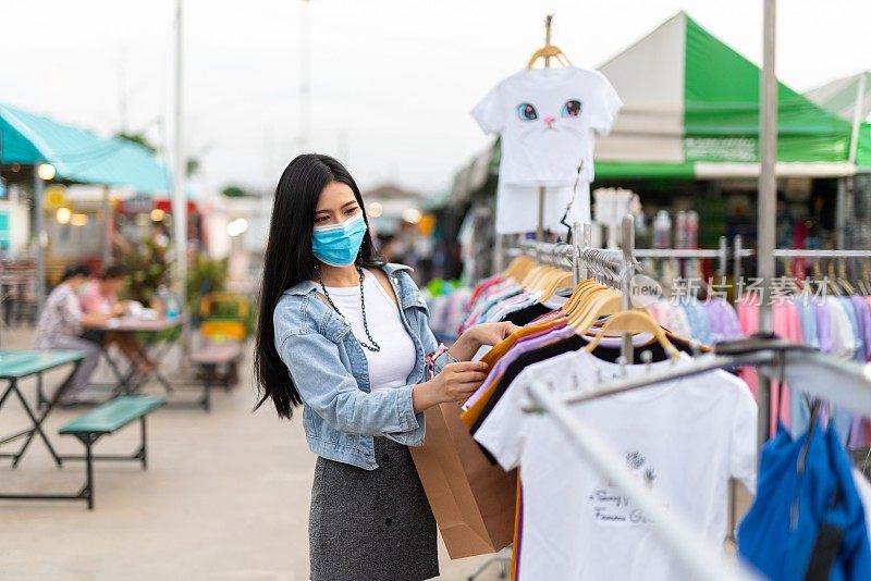 在泰国曼谷当地的夜市，一名戴着防护面膜的女性独自购物