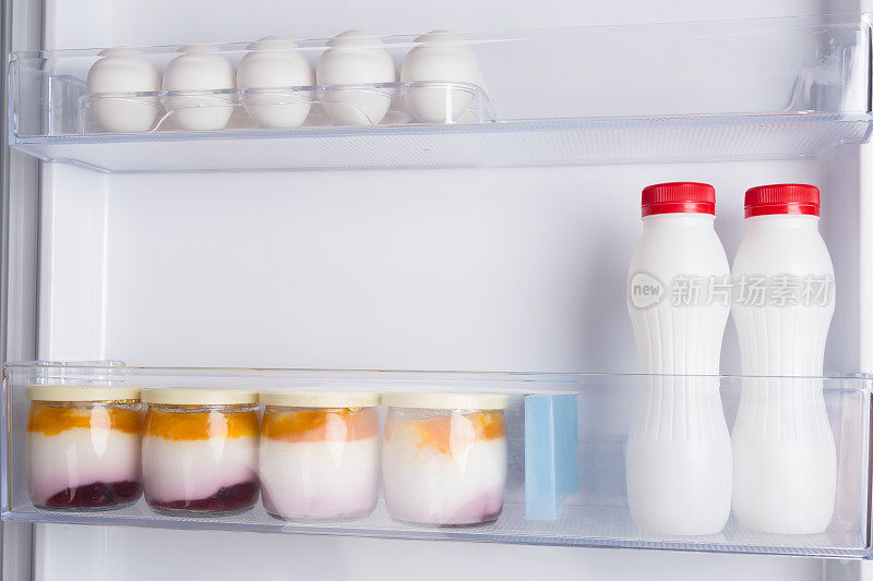 在一个开着的白色冰箱的门上，架子上放着酸奶和鸡蛋